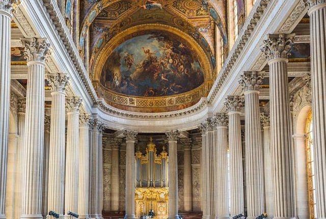 Interior of a grand church with rows of marble columns leading to a gilded altar beneath a large, frescoed dome.