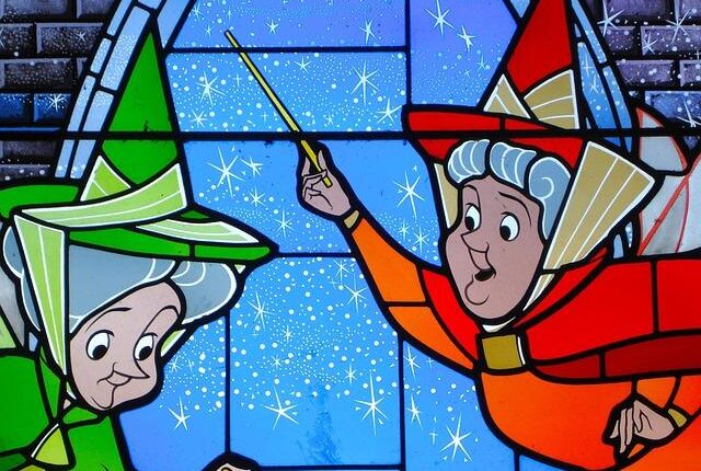 Two whimsical witches in green and red hats point wands at a starry blue stained-glass scene, like window art during winter.